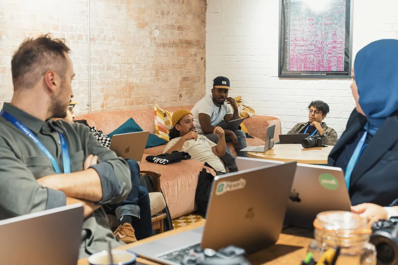 A diverse team sharing ideas and collaborating with laptops around a table — illustrative stock photograph